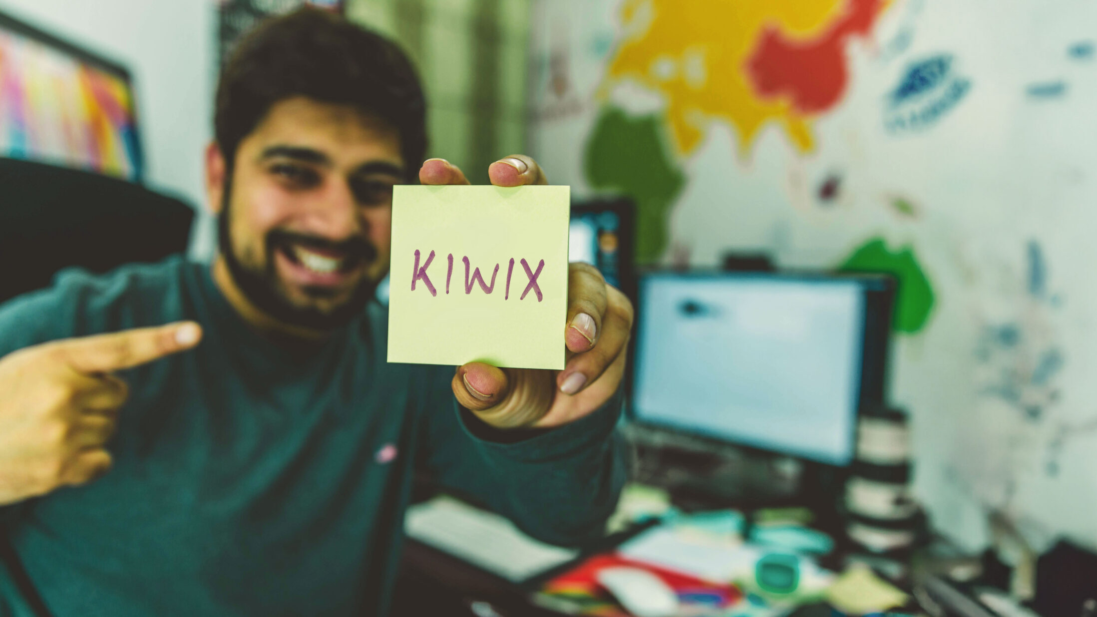Kiwix volunteer coder smiling at camera and holding up a post it with Kiwix written on it.